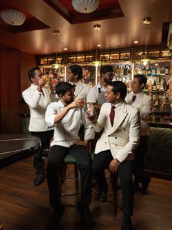 Bartenders in white jackets enjoying craft cocktails in a cozy speakeasy bar with a well-stocked vintage liquor display.
