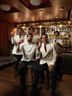 Room 207 staff in white uniforms posing with classic and craft cocktails in a cozy speakeasy bar setting with a well-stocked,