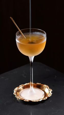 Classic cocktail served in a coupe glass placed on a small ornate gold tray against a dark background