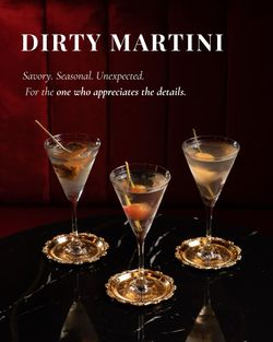 Three dirty martini cocktails served in classic glasses with garnish on a black marble table in a cozy bar setting.