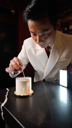 Bartender in a white suit preparing a vintage cocktail at Room 207, a cozy speakeasy bar with craft cocktails.