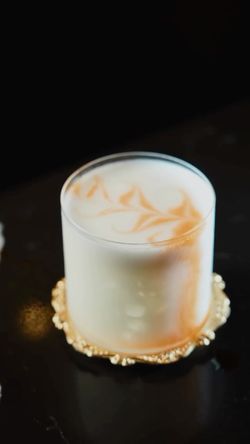 Craft cocktail in a clear glass with a frothy top and ornate golden coaster, set against a dark background at Room 207.