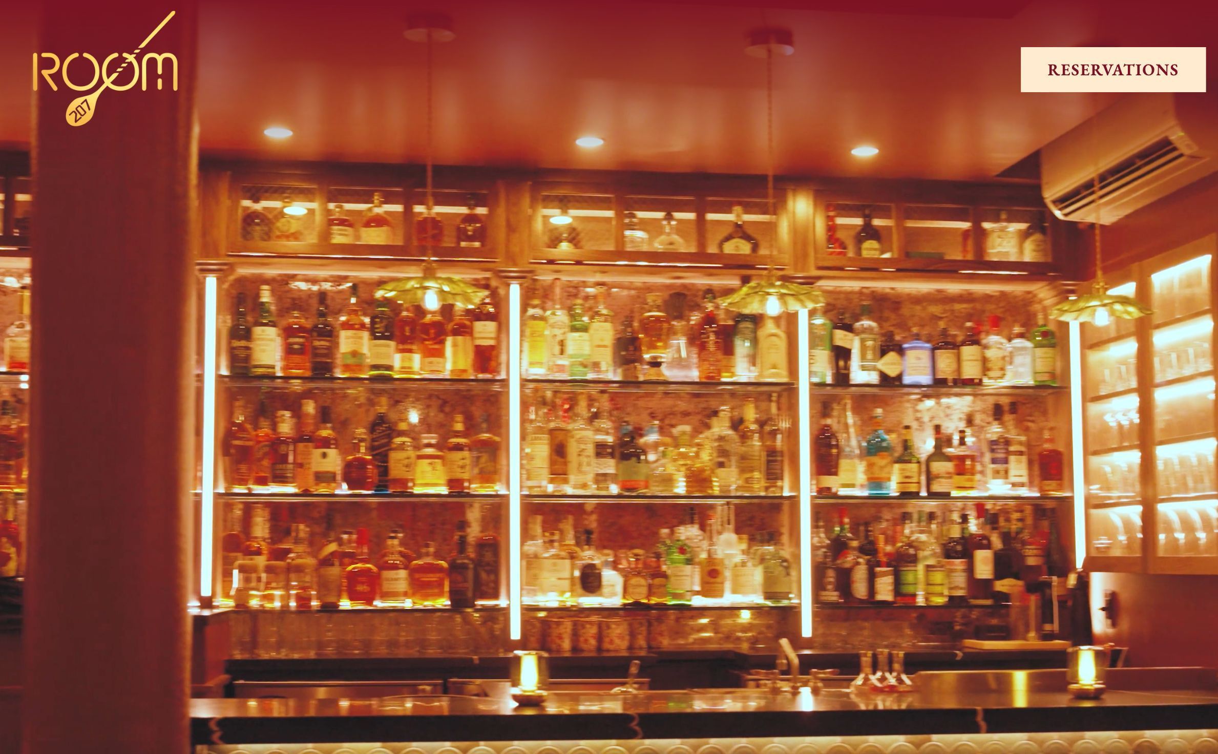 Cozy and warmly lit speakeasy bar at Room 207 featuring a wide selection of classic and vintage spirits on wooden shelves.