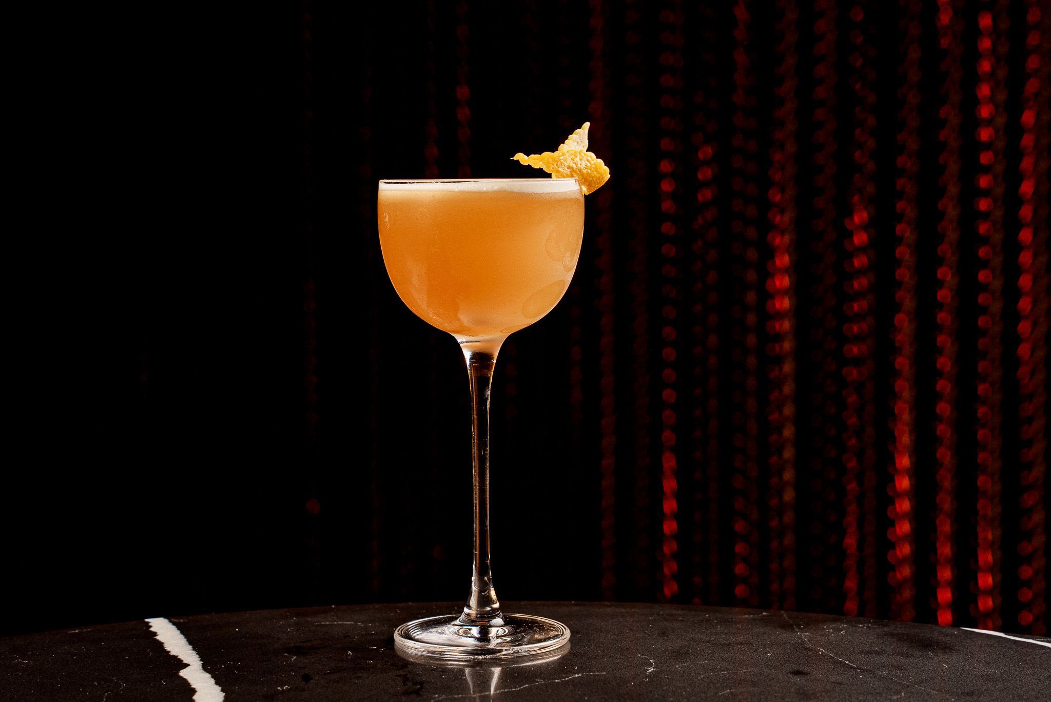Elegant craft cocktail in a coupe glass with a citrus garnish displayed on a black marble table.