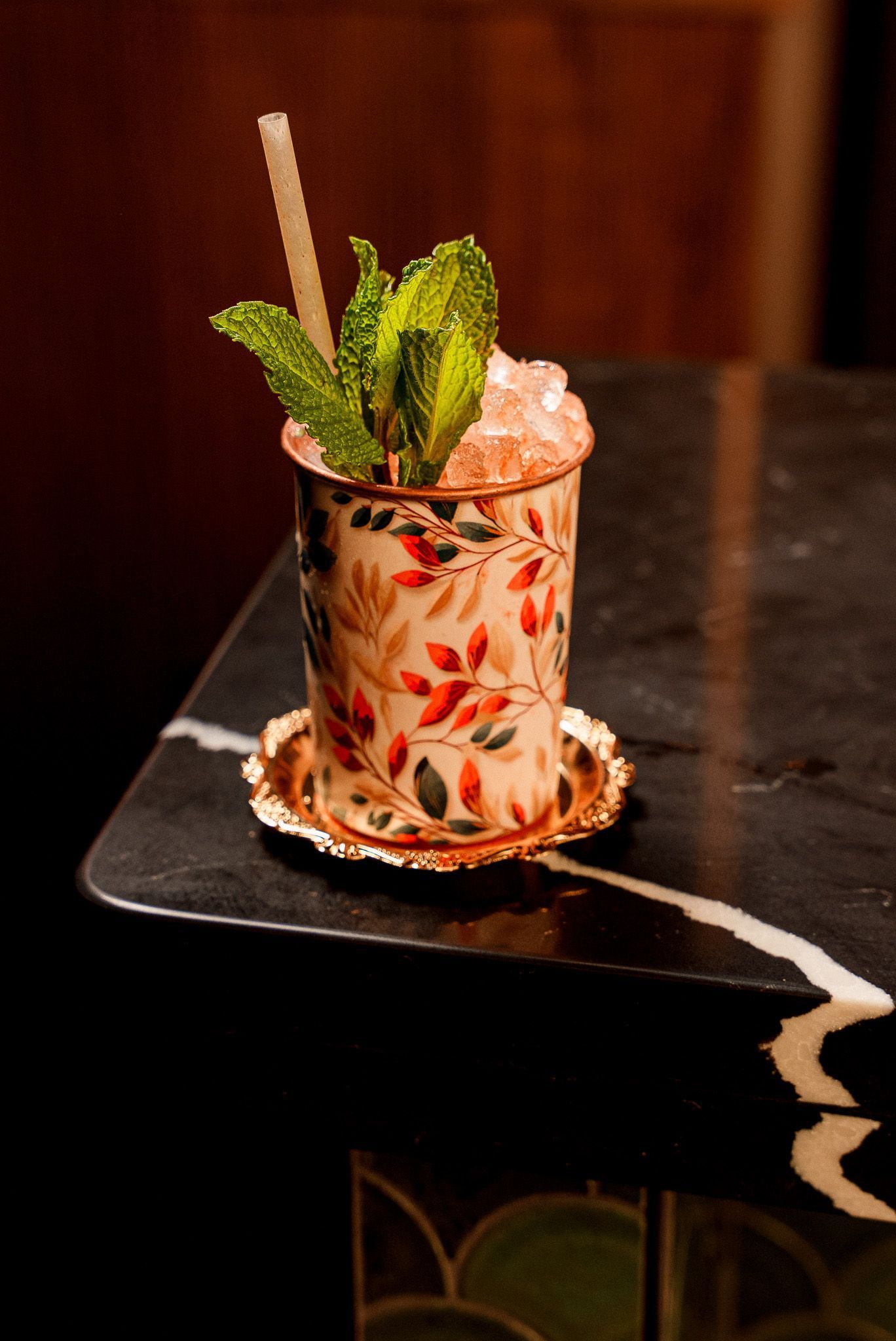 Cocktail in a decorative cup with fresh mint and crushed ice on a dark marble bar surface at Room 207.