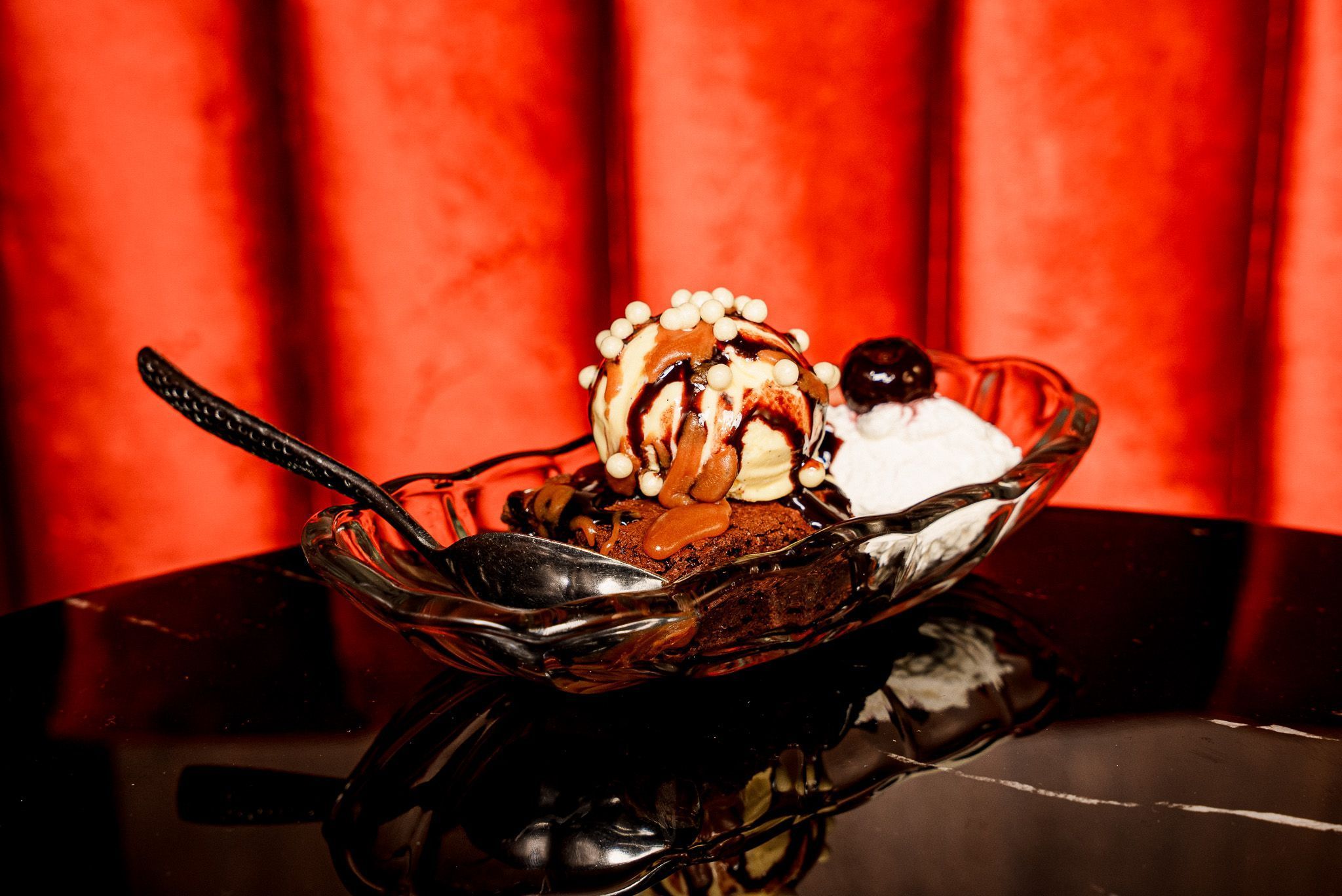 Classic dessert featuring a brownie topped with vanilla ice cream, chocolate syrup, and whipped cream in a glass dish.